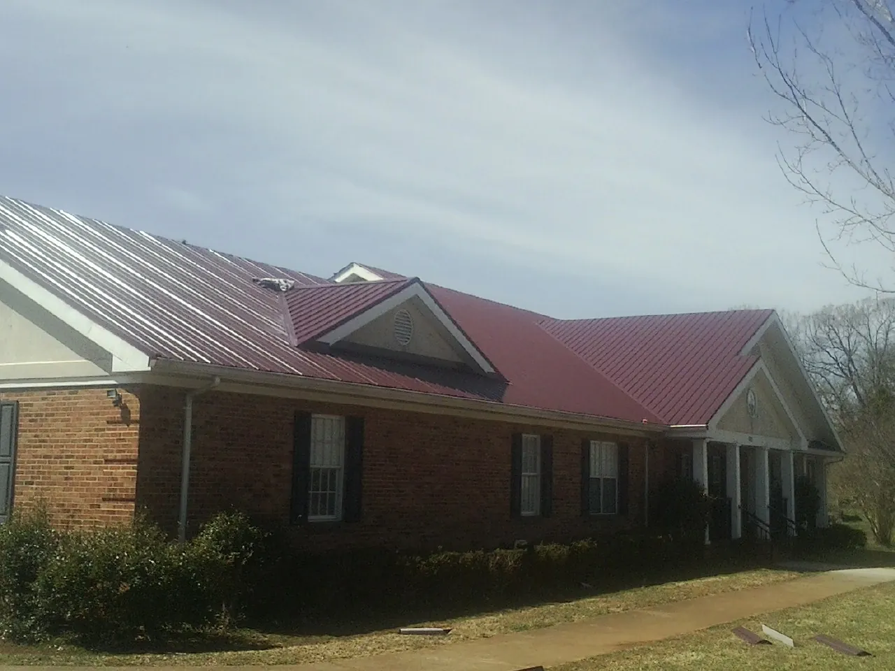 Red metal roof with gabled entries on a long brick building, from a Hail Damage Roof Repair job in Daleville