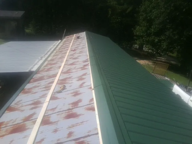 Old rusted panels beside newly installed green metal roofing — Wind Damage Roof Repair by Roofing Brothers in Daleville
