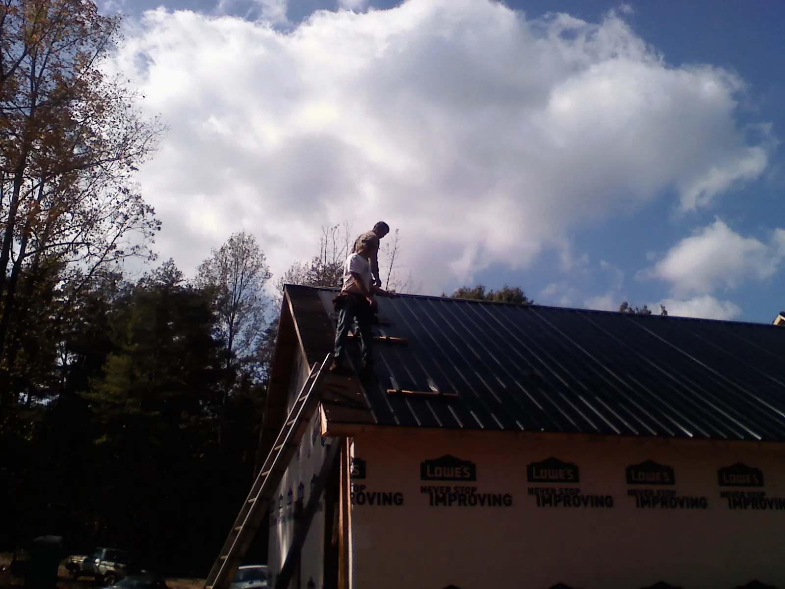 Roofer fastening dark metal panels high against a cloudy sky, from a Roof Inspection job in Daleville